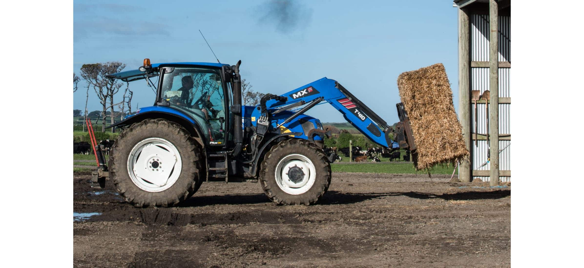 Farm tractor picks up a large hay bale on a farm.